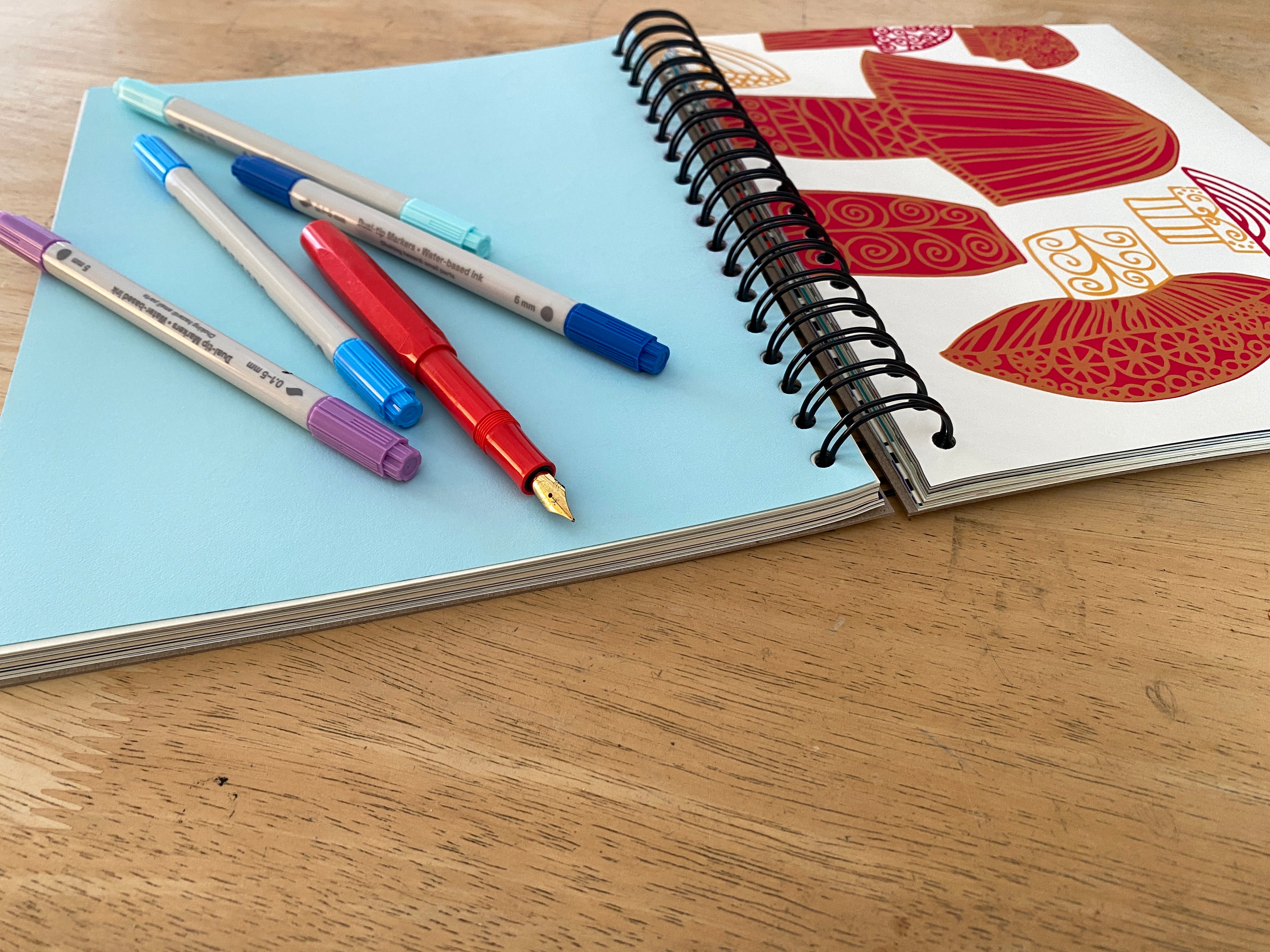 Open notebook with colorful pens on a wooden surface