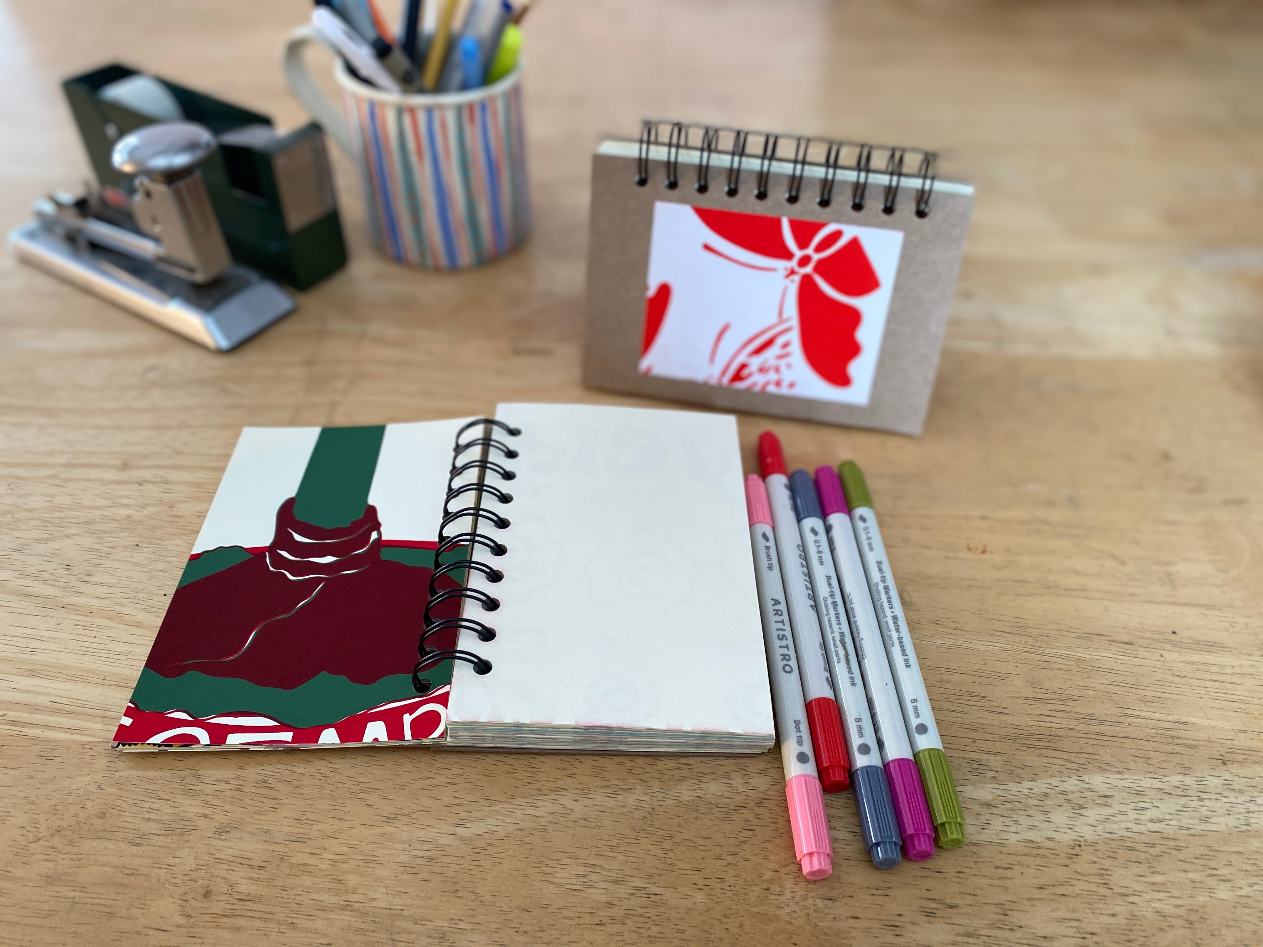 Notebook with colorful cover, pens, and stationery items on a wooden surface