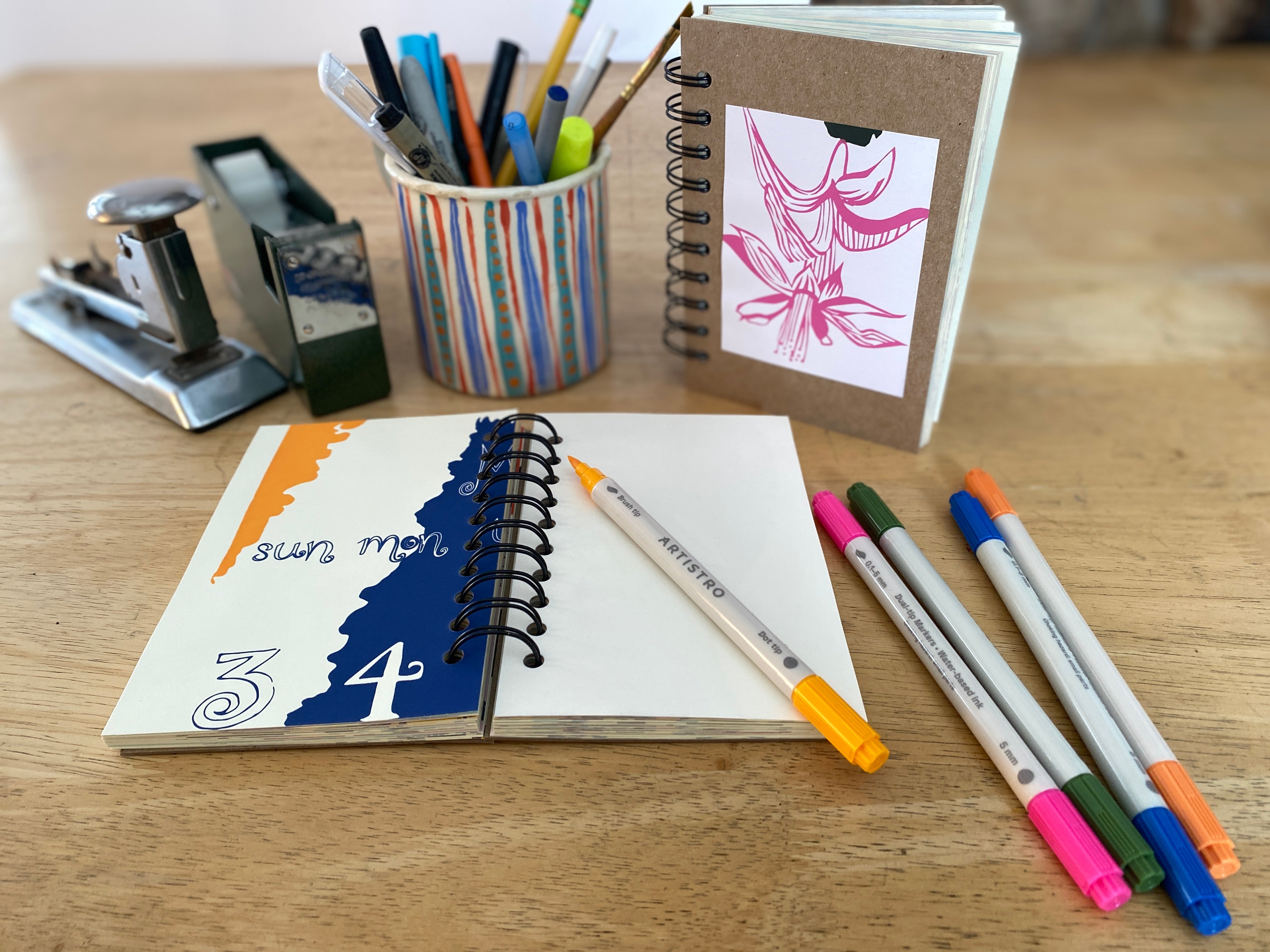 Notebooks and pens on a wooden surface with stationery items.