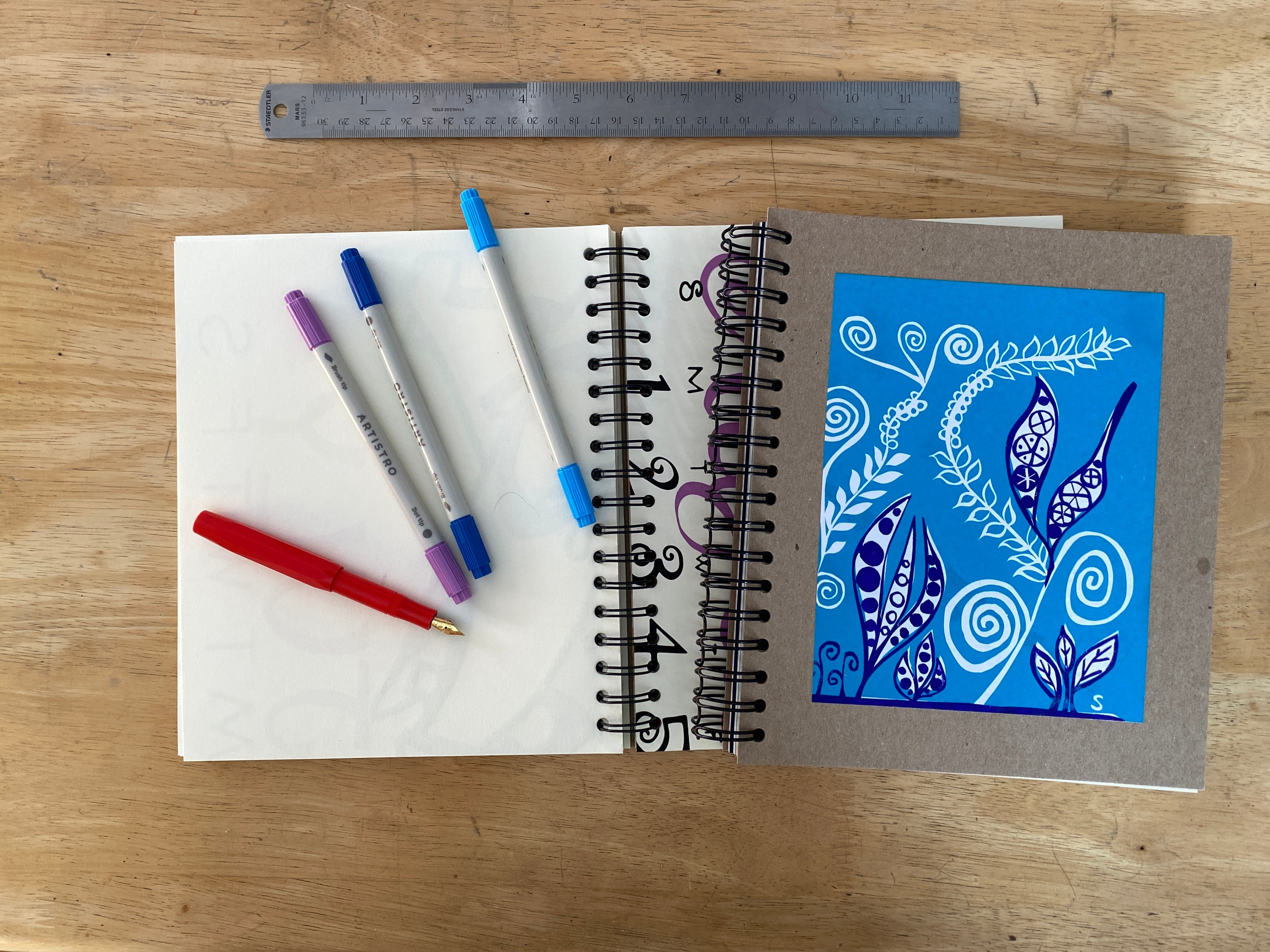 Notebook with colorful pens and a ruler on a wooden surface